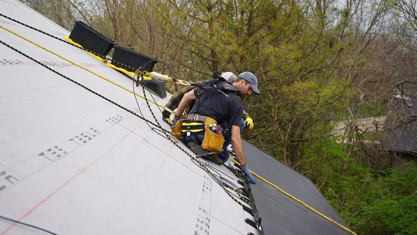 Harnessed roofers installing a new roof above wooded surroundings in Beatrice, Nebraska