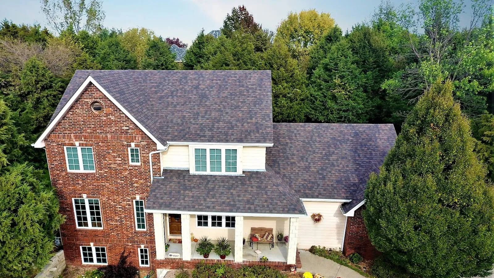 Two story brick Bellevue, Nebraska home with a new architectural shingle roof surrounded by evergreens