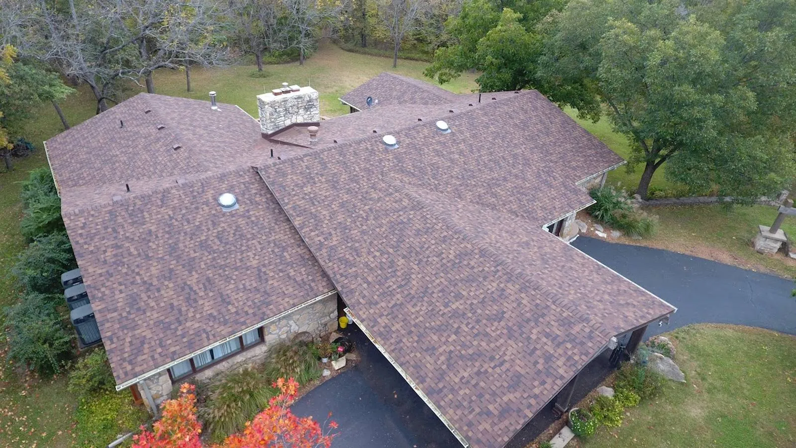 Stone ranch home in Belton, Missouri with a new brown architectural shingle roof surrounded by fall woods