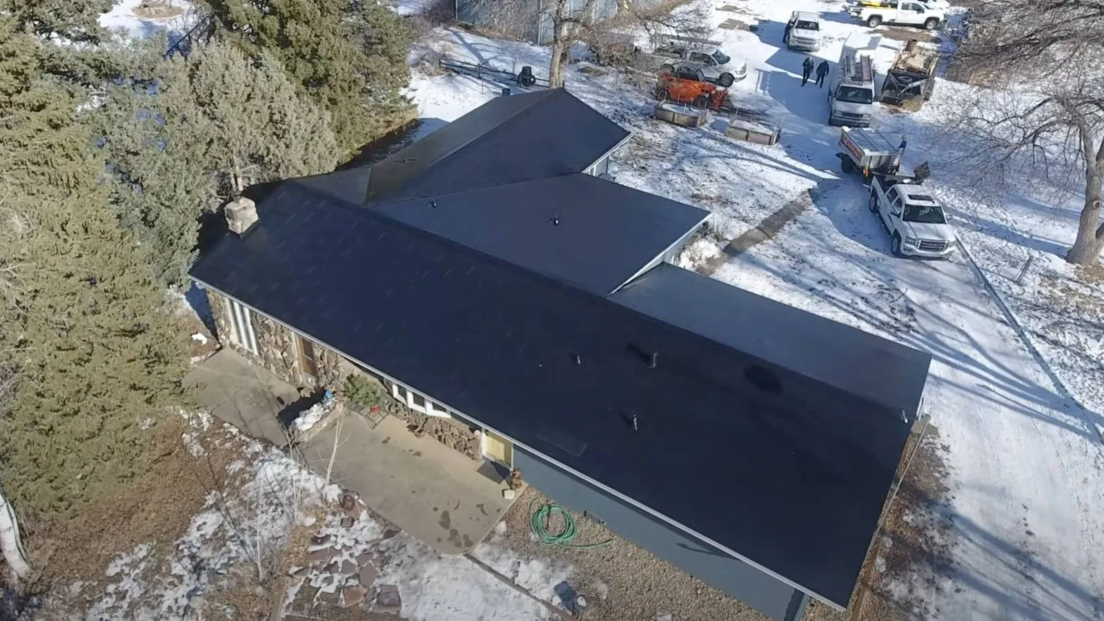 Aerial view of a snowy Berthoud, Colorado area stone home with a new dark solar roof and crew trucks