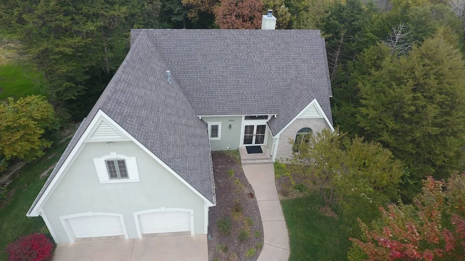 Aerial view of a Blue Springs, Missouri home with a new gray shingle roof and wooded fall backyard