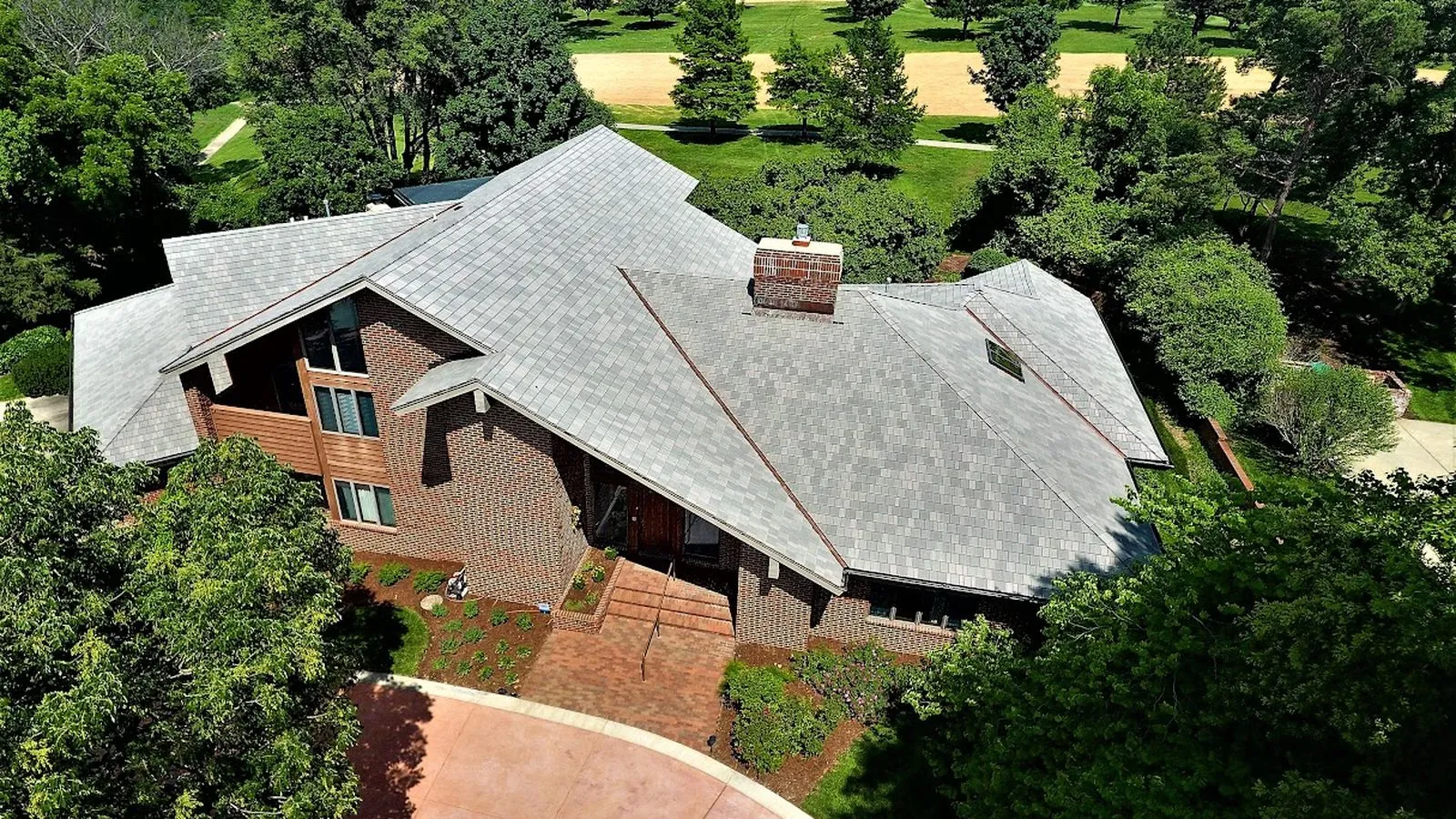 Aerial view of a brick home with a gray slate style roof surrounded by mature trees in Bonner Springs, Kansas