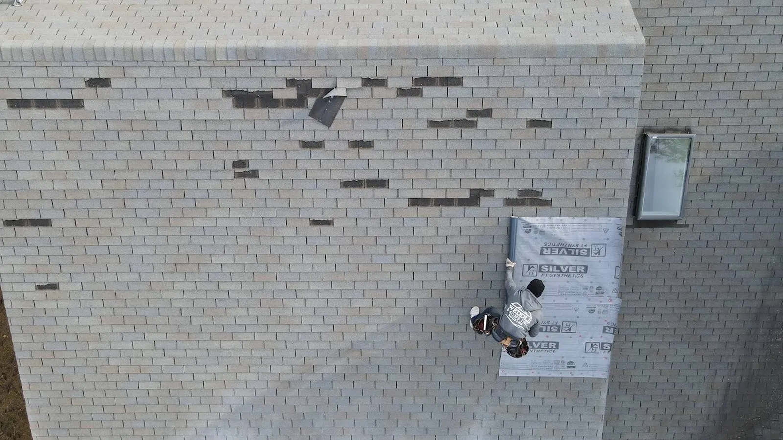 Overhead view of a Weddle and Sons roofer laying synthetic underlayment over wind damaged shingles, serving Brighton, Colorado