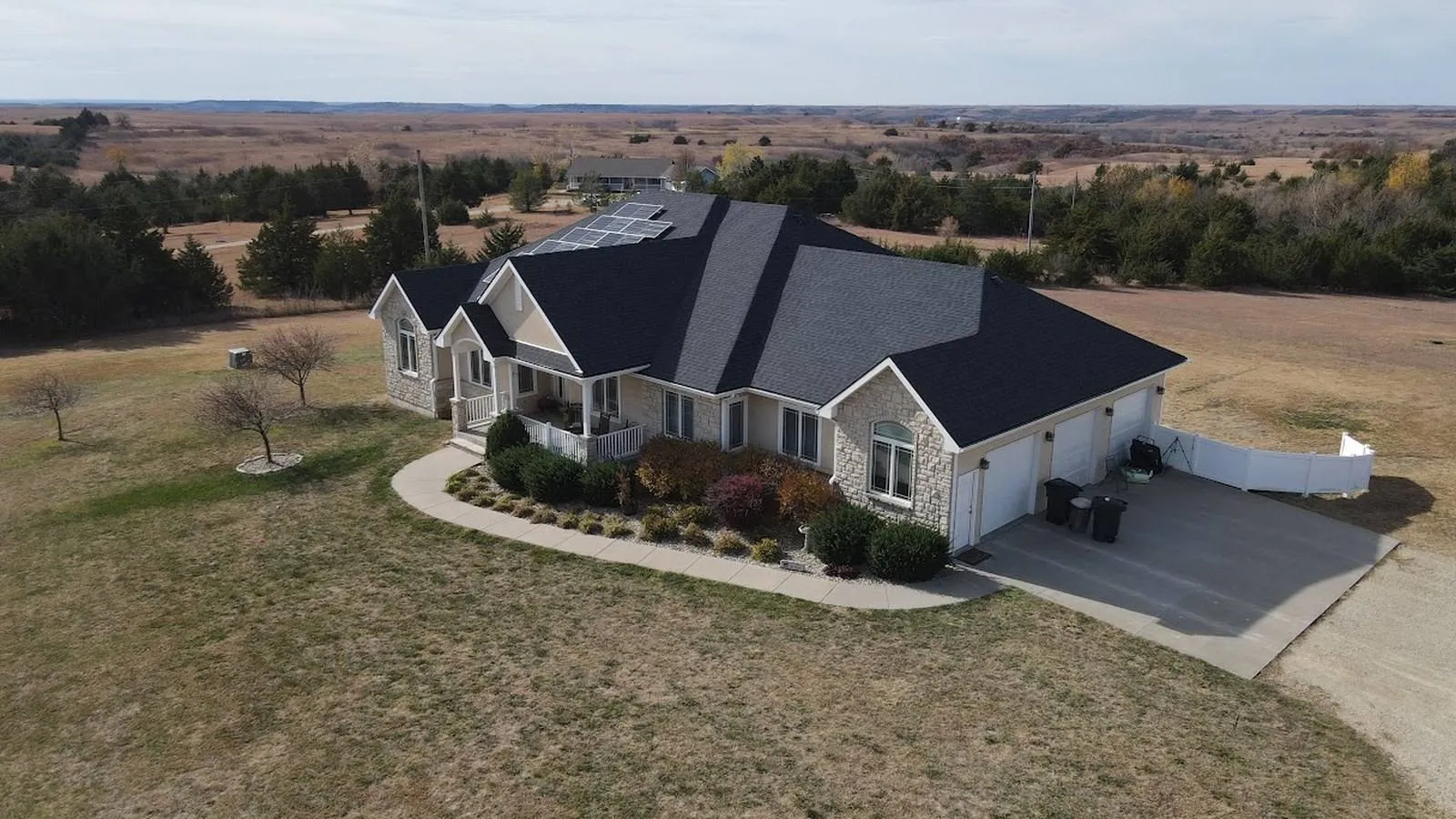 Stone ranch home near Clay Center, Kansas with a new charcoal shingle roof, solar panels, and open prairie beyond