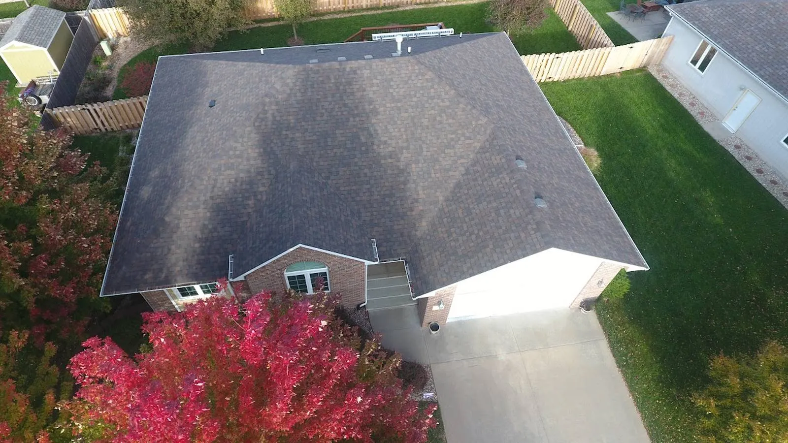 Aerial view of a brick Crete, Nebraska home with a new brown architectural shingle roof beside a red fall maple