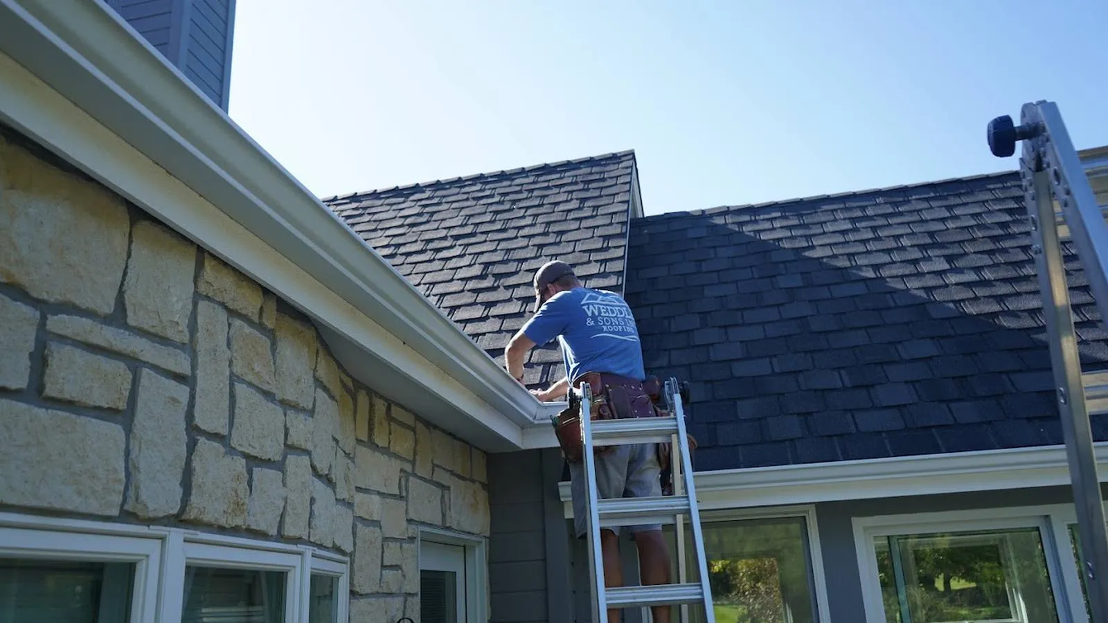 Weddle and Sons installer on a ladder fitting white gutters on a stone home, serving Englewood, Colorado