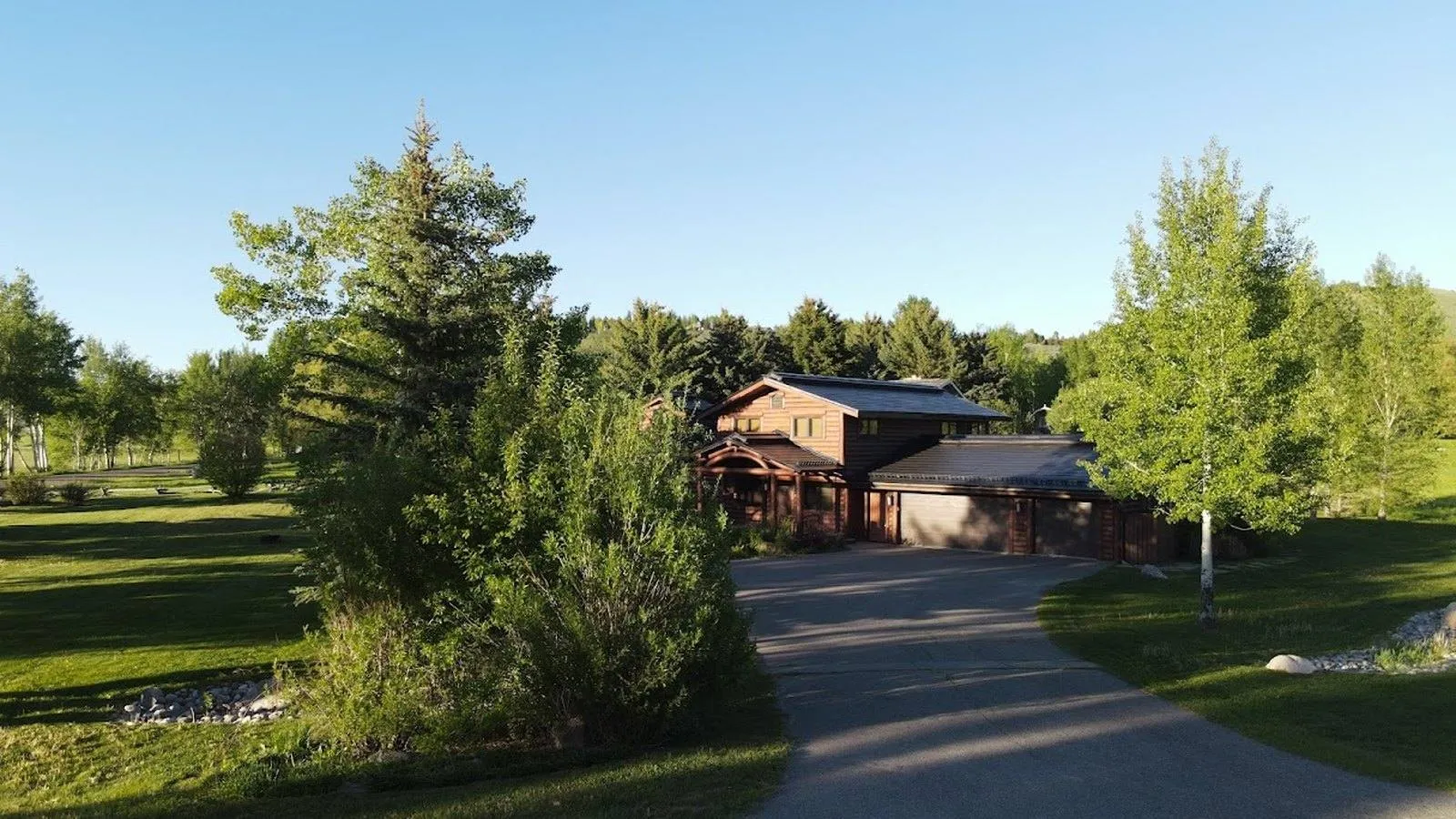 Log home near Grand Lake, Colorado with a dark solar roof, aspens and pines along the driveway