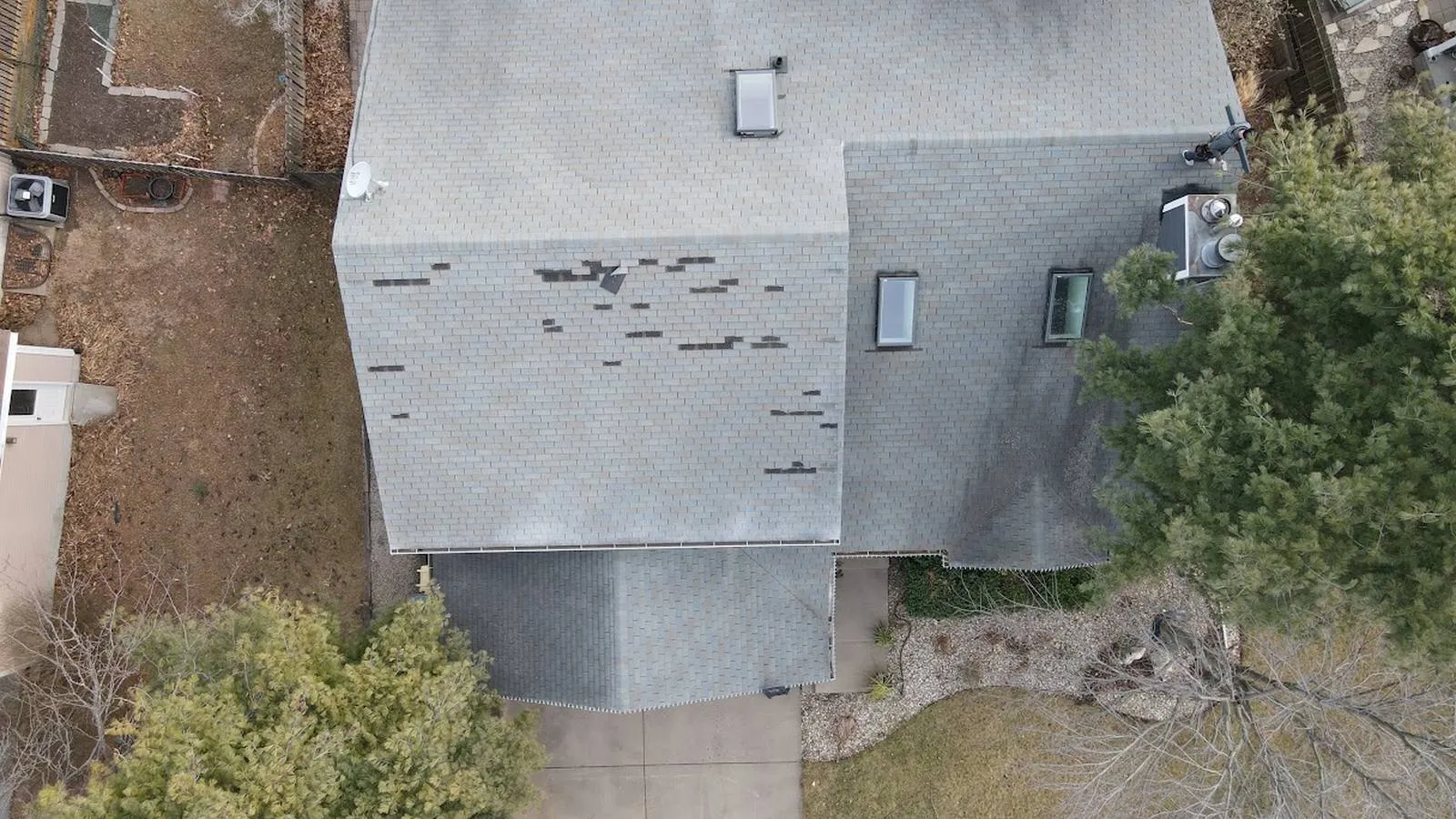 Drone view of a roof with wind blown missing shingles before a storm damage repair, serving Greeley, Colorado