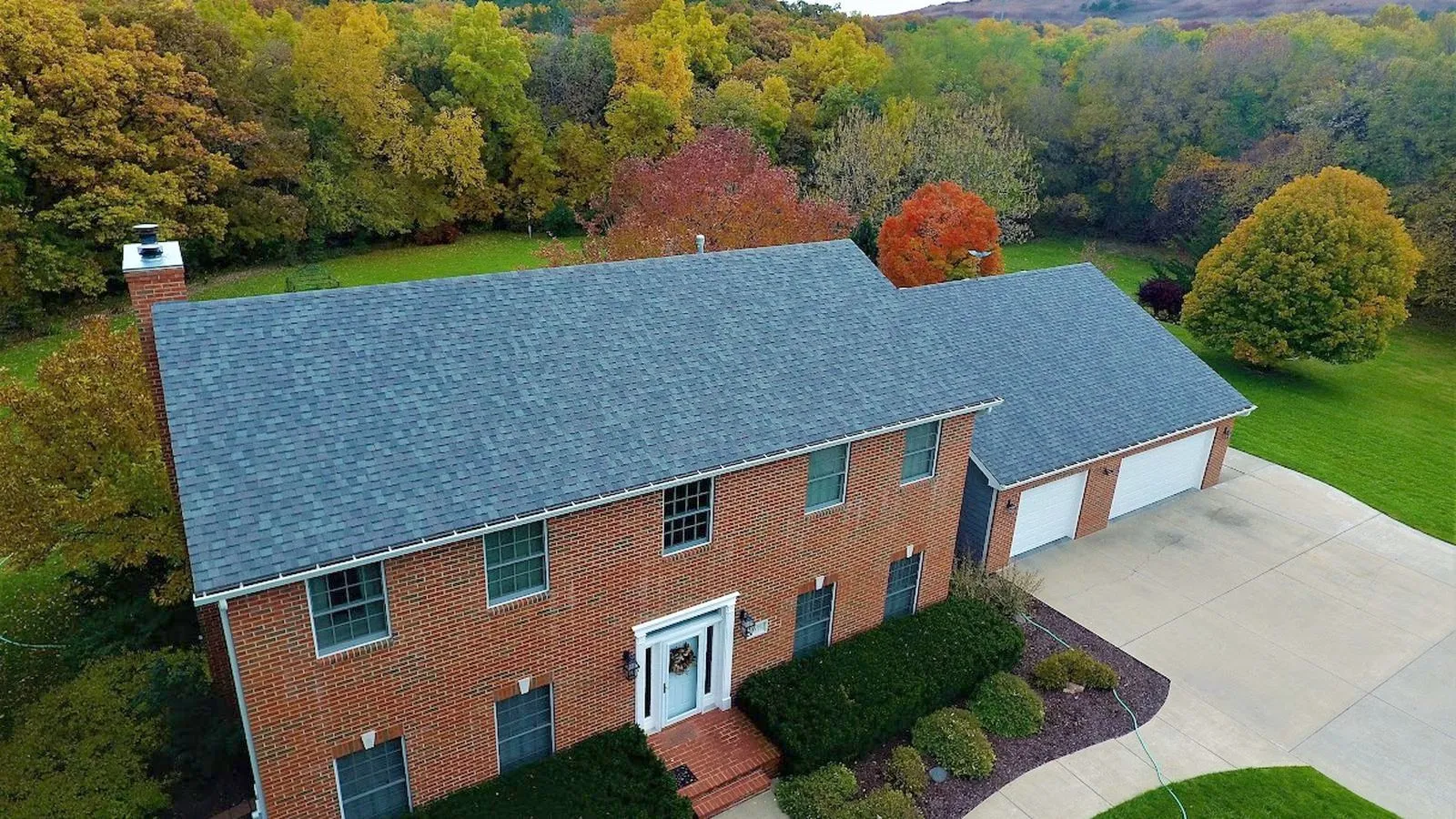 Aerial view of a two story brick home with a new shingle roof and fall trees in Holton, Kansas