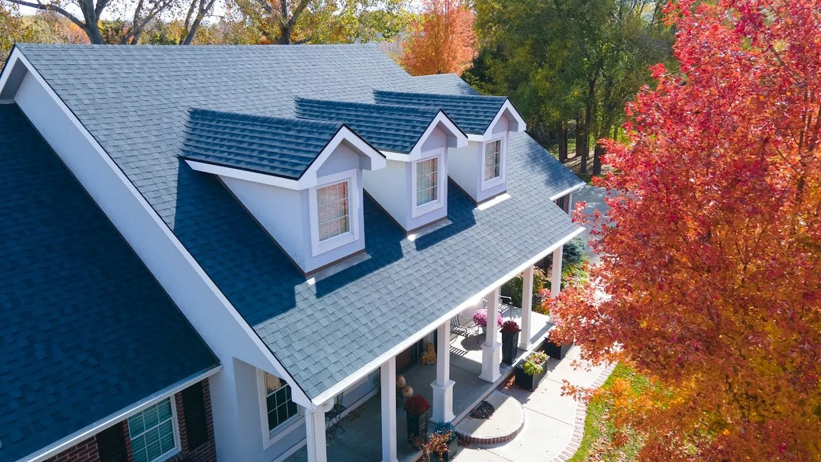 Aerial view of a white two story home with a new architectural shingle roof and covered front porch framed by red and gold autumn trees