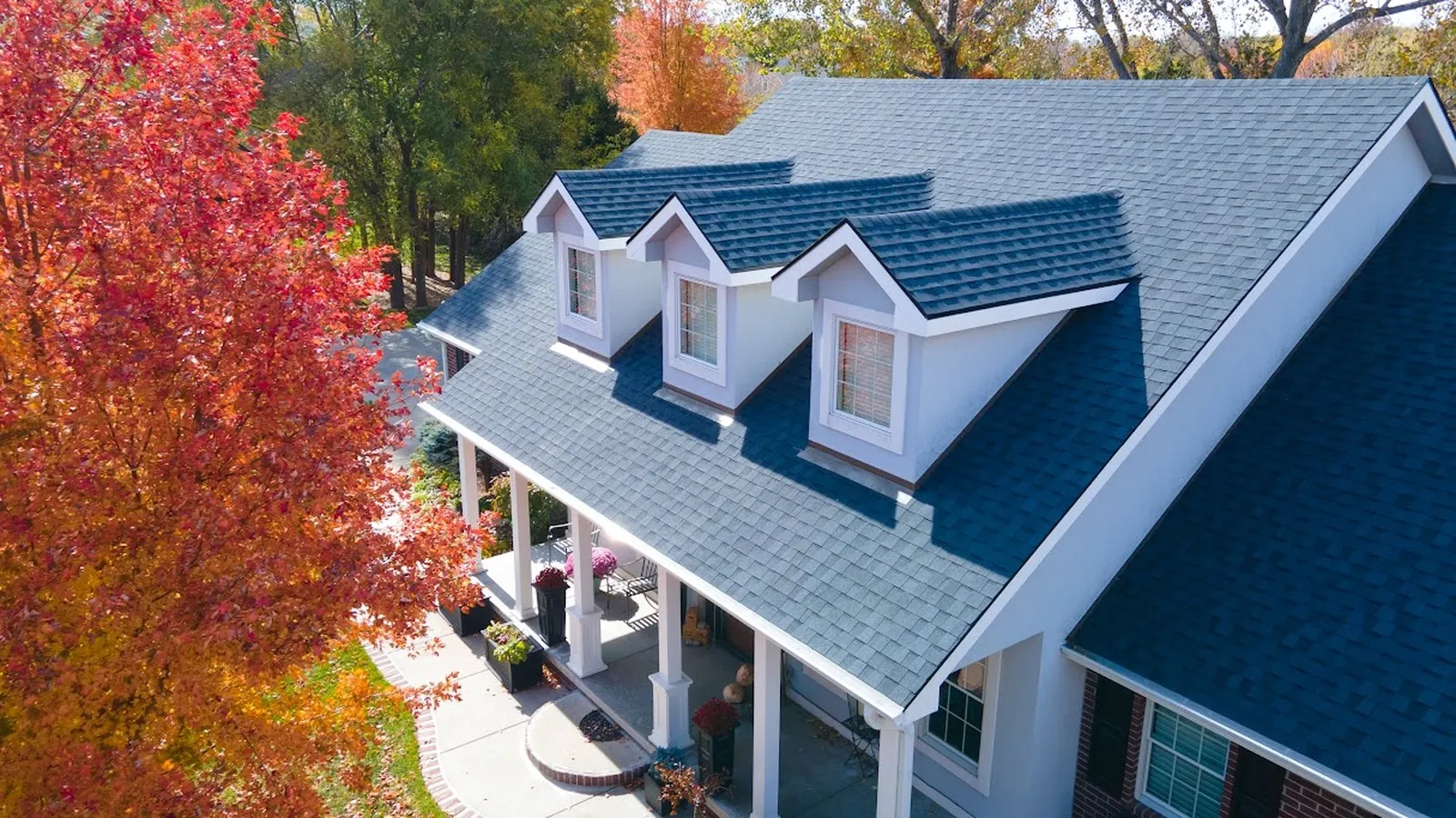 Home with a new architectural shingle roof and covered front porch surrounded by autumn color