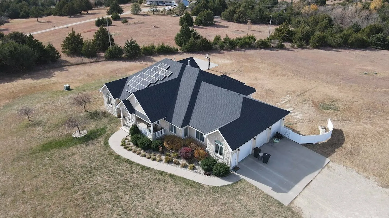 Aerial view of a stone ranch home near Junction City, Kansas with a new charcoal shingle roof and rooftop solar panels above the Flint Hills
