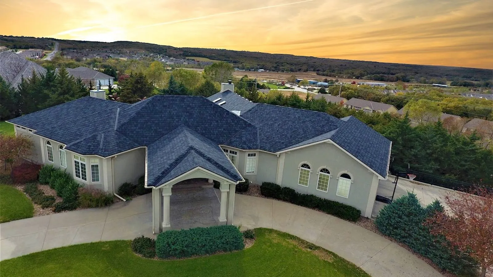 Liberty, Missouri stucco home with a new dark architectural shingle roof overlooking rolling hills at sunset