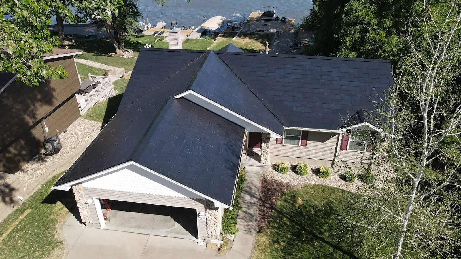Aerial view of a lakefront Louisville, Nebraska home with a new solar shingle roof and dock beyond