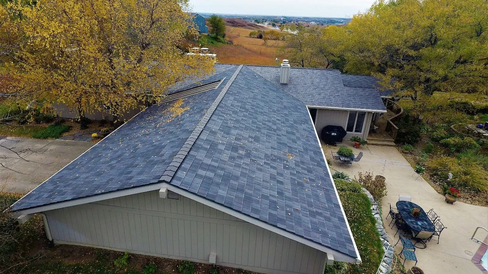 Aerial view of a home with a new dark shingle roof among autumn trees in Marysville, Kansas
