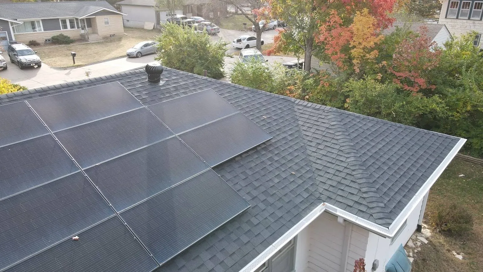 Close aerial view of black solar panels on a new shingle roof at a Merriam, Kansas home with fall color behind it