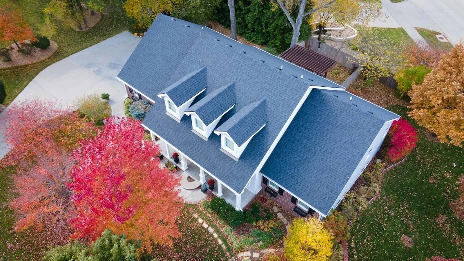 Aerial view of an Overland Park, Kansas home with a new blue gray shingle roof surrounded by autumn trees