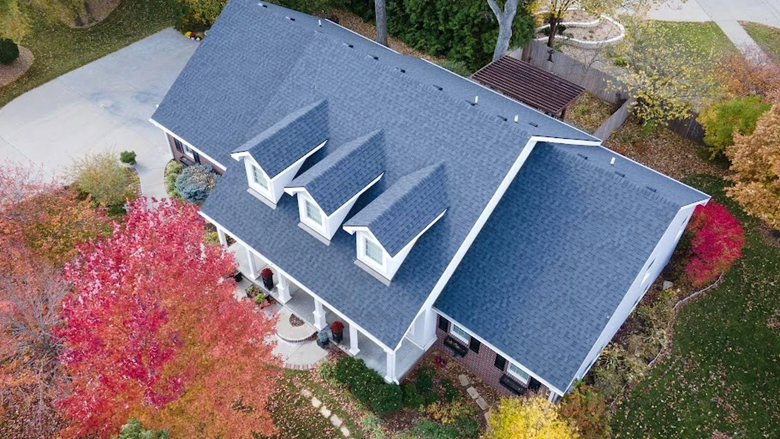 Aerial view of a Prairie Village, Kansas home with a new gray architectural shingle roof, dormer windows and fall color trees