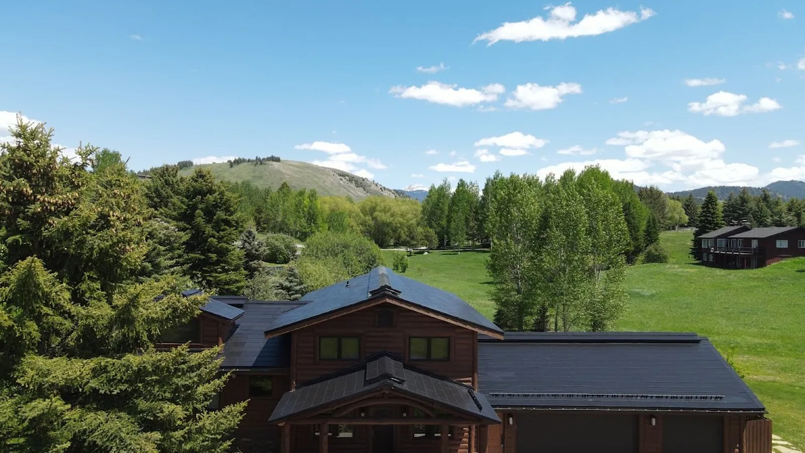 Aerial view of a wood sided home with a new dark solar shingle roof