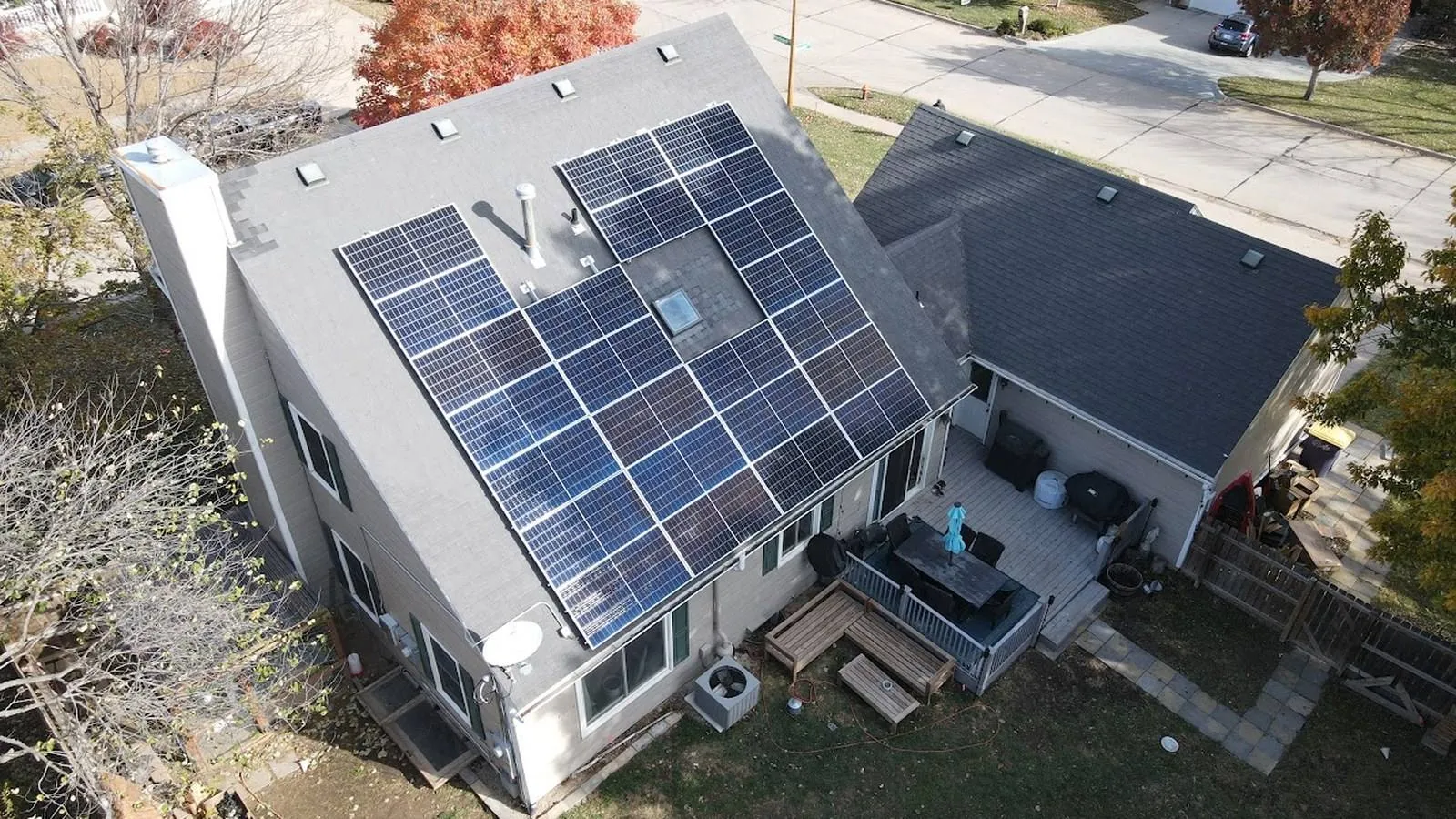 Aerial view of a Shawnee, Kansas home with a new shingle roof and rooftop solar panels framed by fall trees