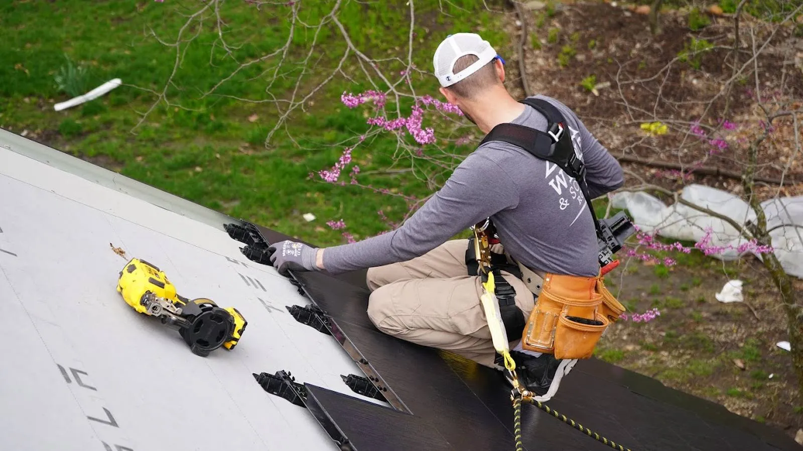 Weddle and Sons roofer installing solar roof tiles above a flowering redbud in Springfield, Nebraska