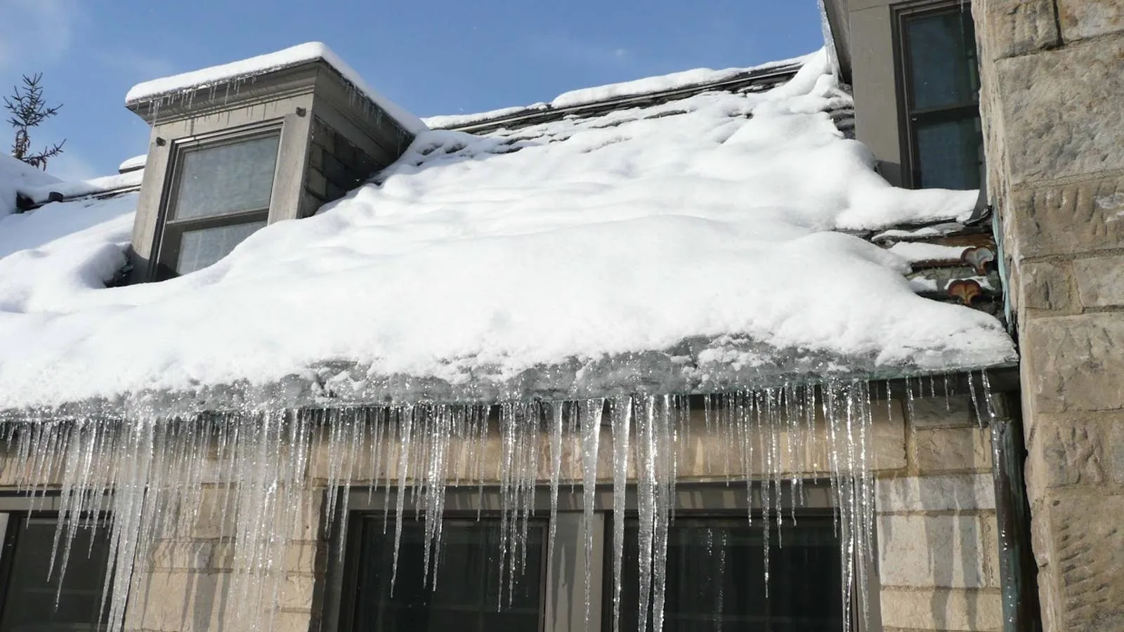 Ice dam and heavy icicles hanging from a snow covered roof edge, a winter problem Weddle and Sons fixes in Wheat Ridge, Colorado