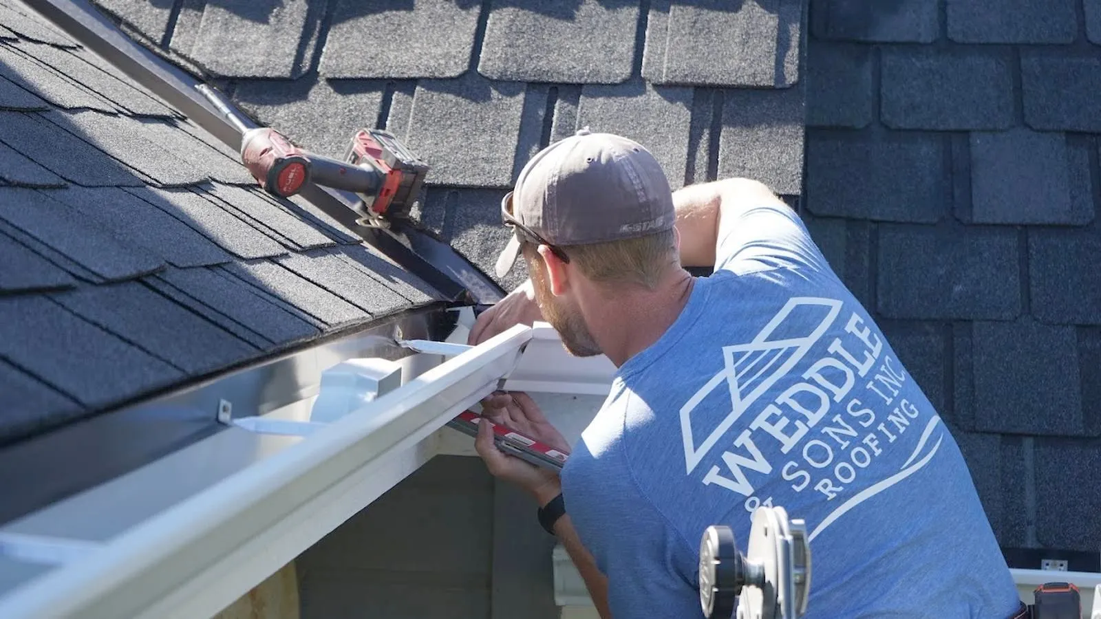 Weddle and Sons installer fastening a new seamless gutter on a shingle roof