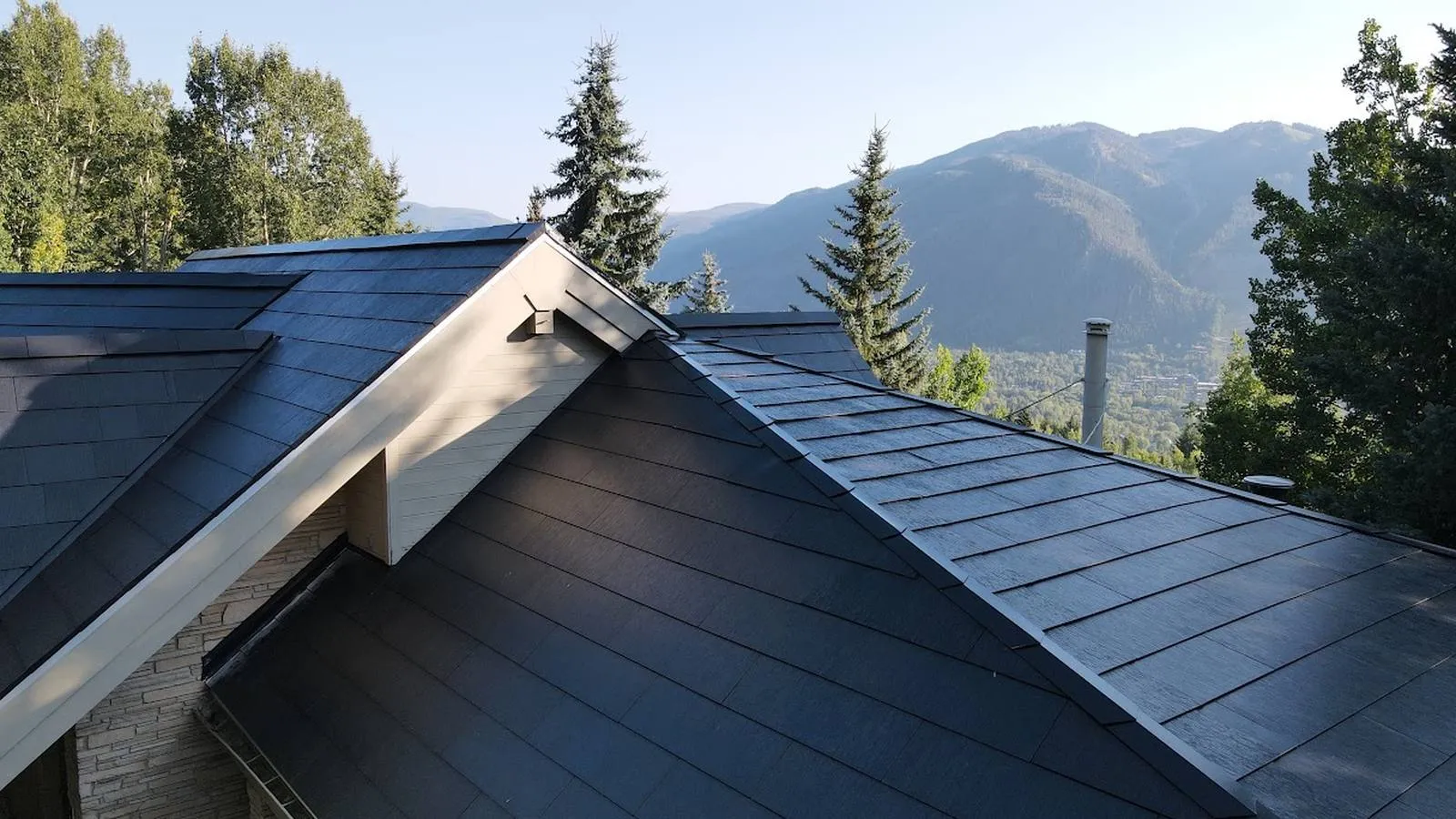 Dark Tesla Solar Roof tiles on a home with pine trees and mountain peaks behind it