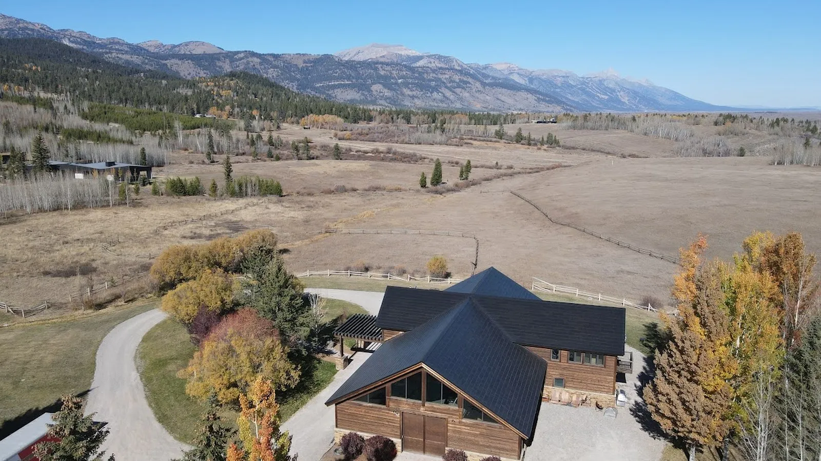 Aerial view of a mountain ranch home with a full solar roof and open pasture beyond it