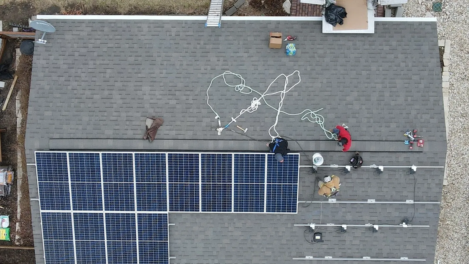 Overhead view of a crew installing rooftop solar panels on a shingle roof