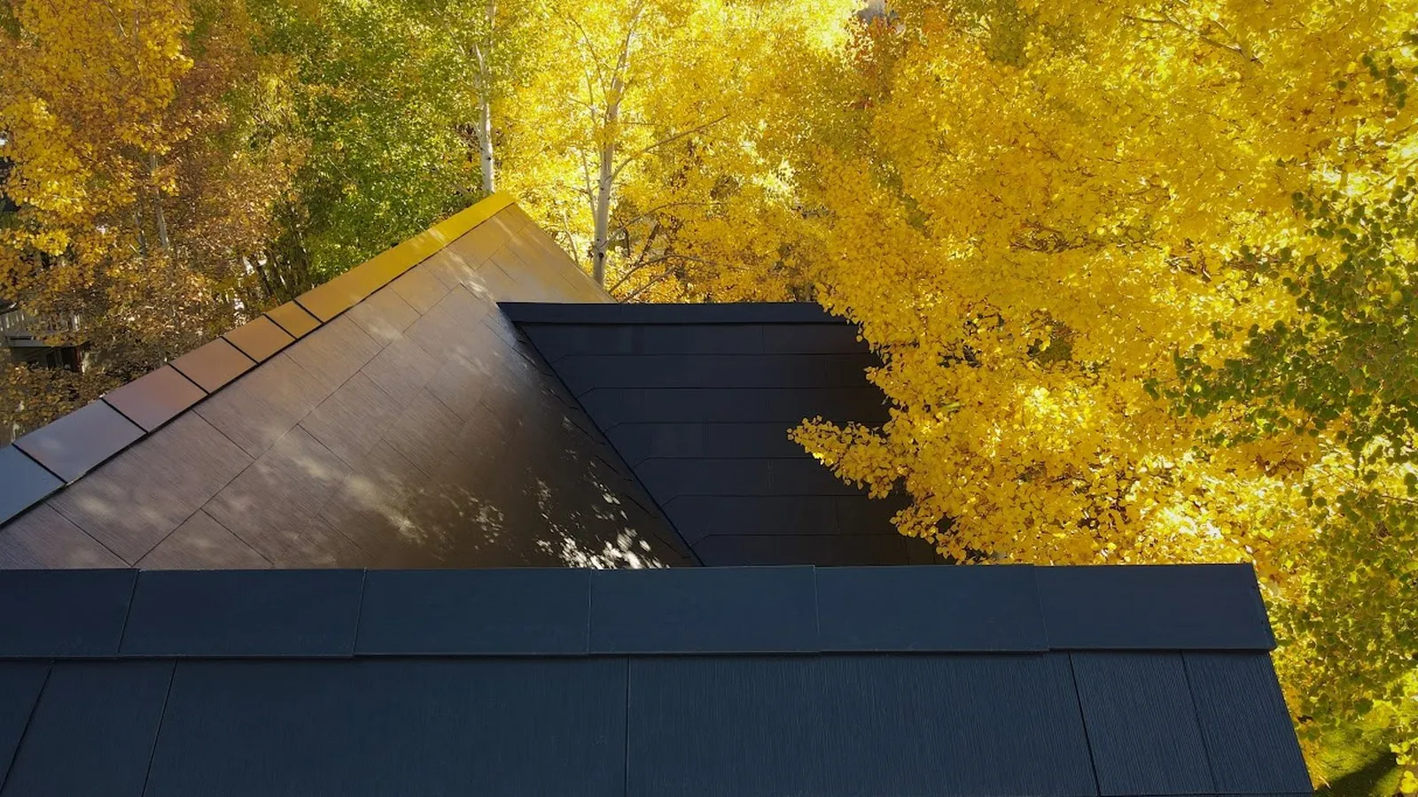 Close view of Tesla Solar Roof tiles on a mountain home framed by golden aspen trees